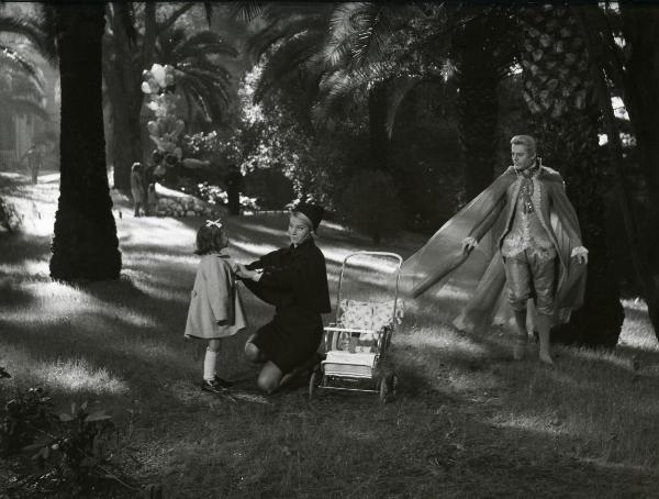 Scena del film "Fantasmi a Roma" - Regia Pietrangeli, Antonio, 1961 - In un parco: Marcello Mastroianni, a destra, osserva in direzione di un'attrice non identificata, in ginocchio, che sistema il cappotto di una giovane attrice non identificata.