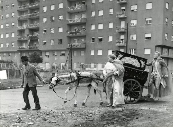 Scena del film "Fantasmi a Roma" - Regia Pietrangeli, Antonio, 1961 - Un attore non identificato, a sinistra, tiene le briglie di un mulo che tira un carretto, su cui appoggia il piede Marcello Mastroianni. Davanti, Tino Buazzelli osserva dietro.