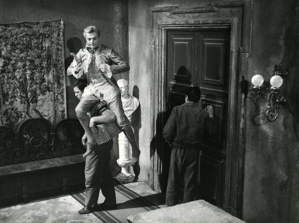 Scena del film "Fantasmi a Roma" - Regia Pietrangeli, Antonio, 1961 - Marcello Mastroianni, al centro, piega le braccia verso il petto ed è seduto sulla spalla sinistra di un attore non identificato.
