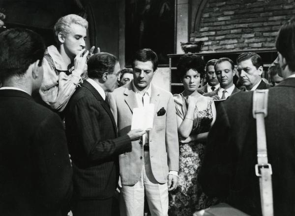 Scena del film "Fantasmi a Roma" - Regia Pietrangeli, Antonio, 1961 - Mastroianni, al centro, Belinda Lee e Gora, a destra, conversano con un attore non identificato che tiene in mano un documento. Dietro, Gassman fa il segno delle corna con le mani.