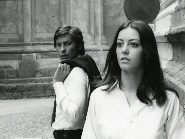 Scena del film "Una farfalla con le ali insanguinate" - Regia Tessari, Duccio, 1971 - In secondo piano, Helmut Berger, tenendosi una giacca sulla spalla, osserva un'attrice non identificata in primo piano che, a sua volta, guarda verso sinistra.