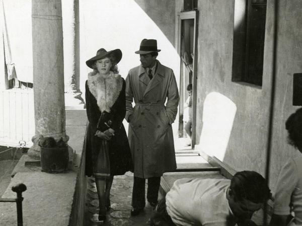 Scena del film "Fari nella nebbia" - Regia Franciolini, Gianni, 1942 - Figure intere di Fosco Giachetti e Mariella Lotti che passeggiano in un corridoio. In primo piano, un attore non identificato è piegato in avanti.