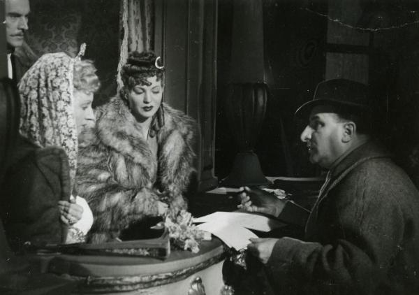 Scena del film "Fedora" - Regia Mastrocinque, Camillo, 1942 - Un attore non identificato, a destra, mostra dei documenti a Luisa Ferida, al centro, e ad un'attrice non identificata, a sinistra. Dietro, Amedeo Nazzari osserva la scena.