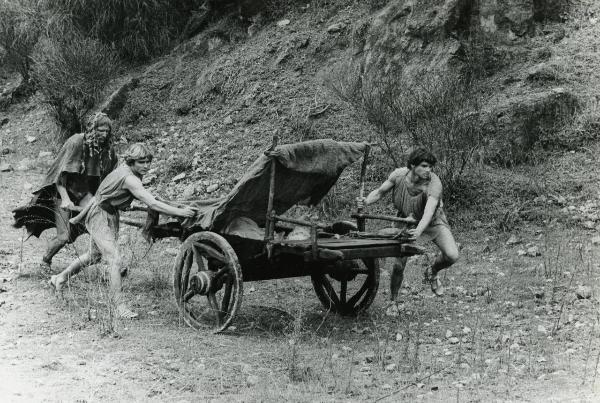 Scena del film "Fellini-Satyricon" - Fellini, Federico, 1969 - Hiram Keller, a destra, Martin Potter, al centro, e un attore non identificato a sinistra spingono un carro di legno su un terreno brullo.