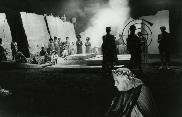 Scena del film "Fellini-Satyricon" - Fellini, Federico, 1969 - Un attore non identificato con una corona di foglie d'oro in primo piano rivolge lo sguardo verso il basso. In secondo piano, numerosi attori non identificati guardano verso l'obbiettivo.