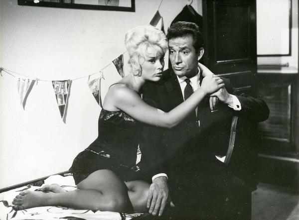 Scena del film "Femmine di lusso" - Bianchi, Giorgio, 1960 - Su un letto: Ugo Tognazzi seduto e un'attrice non identificata si abbracciano e rivolgono lo sguardo verso sinistra.
