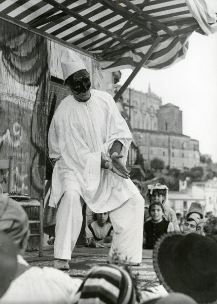 Scena del film "Ferdinando I, Re di Napoli" - Franciolini, Gianni, 1959 - Figura intera di un attore non identificato vestito da Pulcinella che recita su un palcoscenico, osservato da attori e attrici non identificati.
