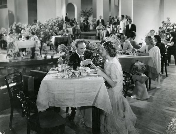 Scena del film "Il feroce Saladino" - Bonnard, Mario, 1937 - Seduti al tavolo di un ristorante: Angelo Musco, a sinistra, porta alla bocca di un'attrice non identificata, sorridente a destra, una forchetta con del cibo.
