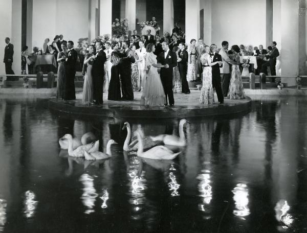 Scena del film "Il feroce Saladino" - Bonnard, Mario, 1937 - Coppie di attori non identificati, tra cui si può riconoscere Lino Carenzio in centro, sono intenti a ballare. In secondo piano, attori non identificati conversano e suonano.
