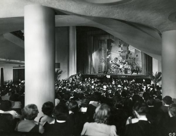 Scena del film "Il feroce Saladino" - Bonnard, Mario, 1937 - Rosina Anselmi e due attori non identificati su un palcoscenico in abiti marinareschi, recitano. Davanti a loro numerosi attori non identificati osservano lo spettacolo.
