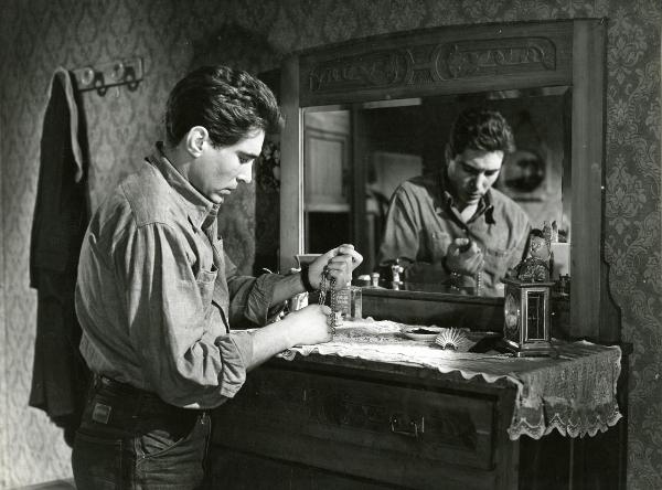 Scena del film "Il ferroviere" - Germi, Pietro, 1956 - In una camera da letto: Renato Speziali, appoggiato a un comò e riflesso in uno specchio, è intento a osservare una collana.
