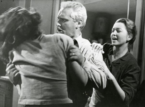 Scena del film "Il ferroviere" - Germi, Pietro, 1956 - Pietro Germi adirato, al centro, trattiene saldamente le spalle di un'attrice non identificata girata di schiena. Intanto, Luisa Della Noce, a destra, gli afferra il braccio sinistro.

