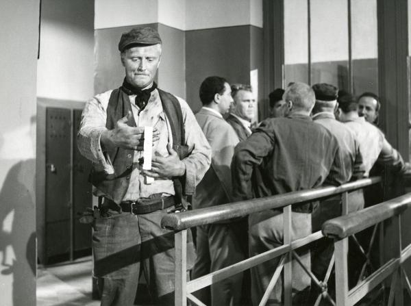 Scena del film "Il ferroviere" - Germi, Pietro, 1956 - Mezza figura di Pietro Germi, a sinistra, che controlla l'oggetto non identificato che tiene tra le mani. In secondo piano è presente un gruppo di attori non identificati.
