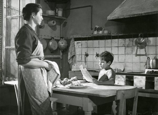 Scena del film "Il ferroviere" - Germi, Pietro, 1956 - In una cucina: Edoardo Nevola, a sinistra è intento a leggere una pagella scolastica, intanto, Luisa Della Noce, a sinistra, asciugandosi le mani in uno strofinaccio, lo osserva.
