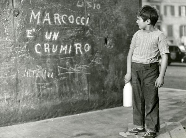 Scena del film "Il ferroviere" - Germi, Pietro, 1956 - Figura intera di Edoardo Nevola con in mano una bottiglia bianca, intento a leggere un muro che riporta la scritta "Marcocci é un crumiro".