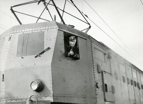 Scena del film "Il ferroviere" - Germi, Pietro, 1956 - Dal finestrino di una cabina motrice di un treno appare Pietro Germi, in divisa da ferroviere, che gesticola e rivolge lo sguardo verso l'obbiettivo.
