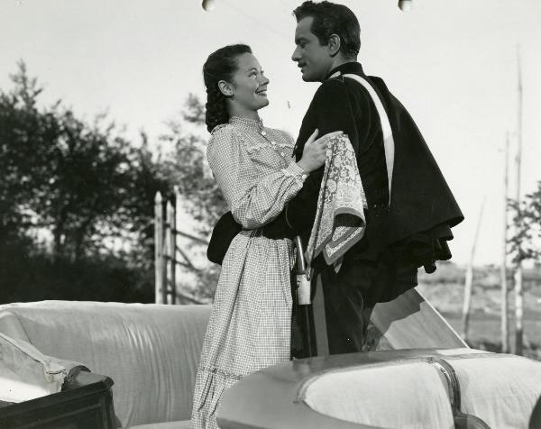 Scena del film "Fiamma che non si spegne" - Cottafavi, Vittorio, 1949 - In piedi su un veicolo di trasporto: Maria Denis con un fazzoletto in mano e Leonardo Cortese in abiti da carabiniere si stringono in un abbraccio e si sorridono.
