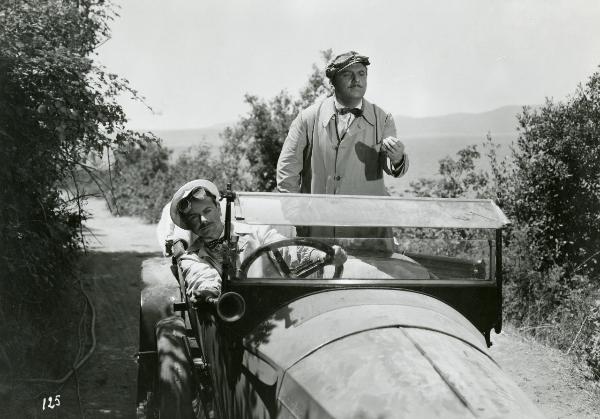 Scena del film "Fiamma che non si spegne" - Cottafavi, Vittorio, 1949 - Su un automobile d'epoca, Gino Cervi, a destra, gesticola con la mano e guarda avanti. A sinistra, un attore non identificato è alla guida e, sporgendosi guarda davanti a sé.