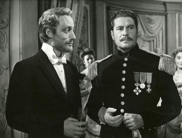 Scena del film "La fiammata" - Blasetti, Alessandro, 1952 - Rolf Tasna, a sinistra con un bicchiere in mano, osserva Amedeo Nazzari, a destra in abiti militari che rivolge lo sguardo a destra.

