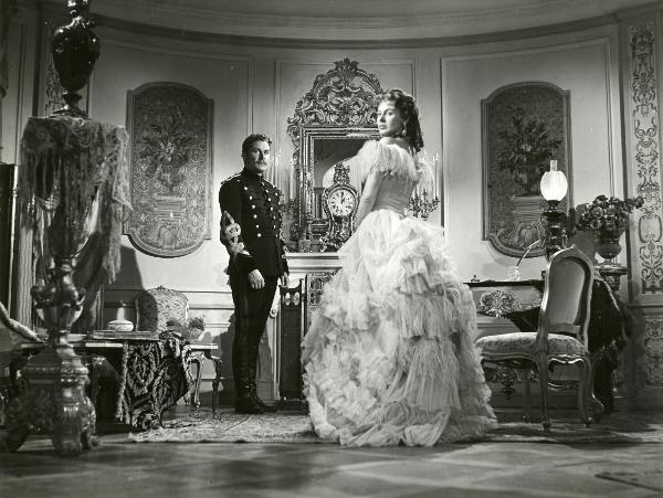 Scena del film "La fiammata" - Blasetti, Alessandro, 1952 - Eleonora Rossi Drago, a destra in primo piano in abito elegante, e Amedeo Nazzari, a sinistra in secondo piano in vesti militari, rivolgono lo sguardo verso l'obbiettivo.
