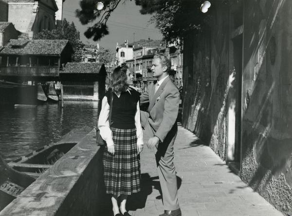 Scena del film "Fiamme sulla laguna" - Scotese, Giuseppe Maria, 1951 - Con alle spalle un paesaggio veneziano, Lea Padovani, a sinistra, osserva Leonardo Cortese che, appoggiando il piede destro a un muretto, le parla.
