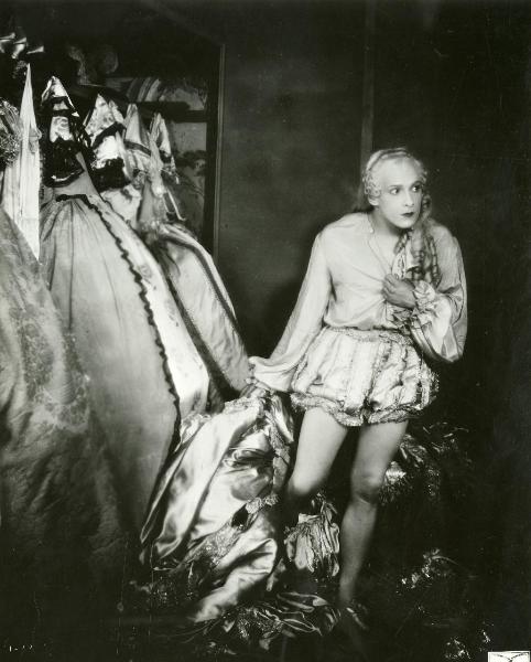 Scena del film "Figaro e la sua gran giornata" - Camerini, Mario, 1931 - Figura intera di un'attrice non identificata che, stringendosi la camicia con la mano sinistra per coprirsi, si toglie un vestito voluminoso attraverso le gambe.
