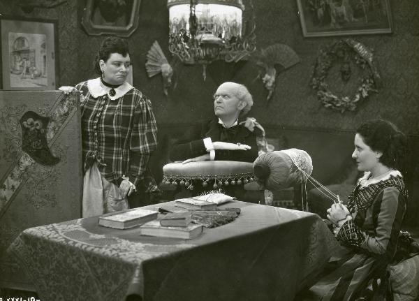 Scena del film "Figaro e la sua gran giornata" - Camerini, Mario, 1931 - Olga Capri, a sinistra, e Gianfranco Giachetti, al centro, si guardano. Intanto un'attrice non identificata, seduta a destra intenta a lavorare il tombolo, li osserva.