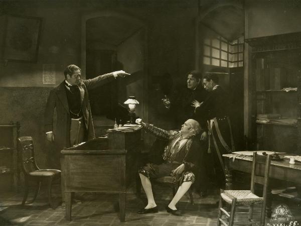 Scena del film "Figaro e la sua gran giornata" - Camerini, Mario, 1931 - Un attore non identificato in piedi a sinistra fa segno di uscire a due attori non identificati, in secondo piano. Intanto al centro, un attore non identificato lo osserva.