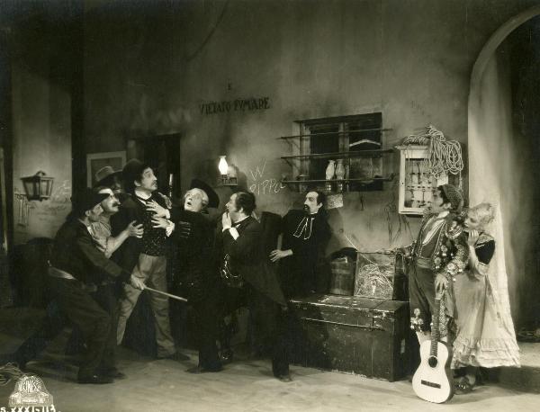 Scena del film "Figaro e la sua gran giornata" - Camerini, Mario, 1931 - Un attore non identificato viene trattenuto da attori non identificati che lo circondano. A destra, un attore non identificato e Gloria Leda lo guardano impauriti.