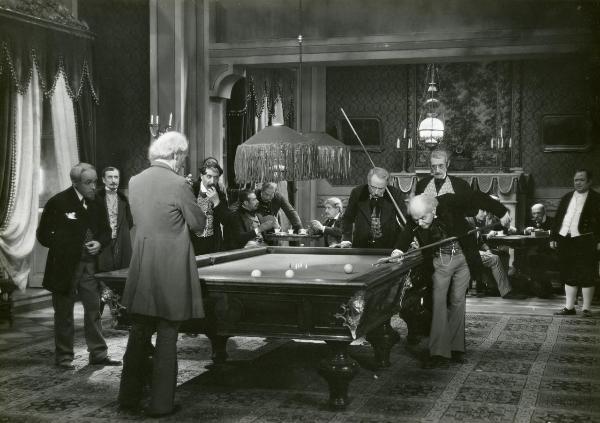 Scena del film "Figaro e la sua gran giornata" - Camerini, Mario, 1931 - In una sala, Gianfranco Giachetti, a destra chino, gioca a biliardo. Tutt'intorno a lui attori non identificati lo osservano.
