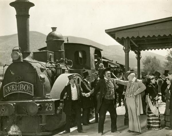 Scena del film "Figaro e la sua gran giornata" - Camerini, Mario, 1931 - Giafranco Giachetti appoggia una mano sulla spalla di un attore non identificato a braccia aperte. Un attore non identificato, a sinistra in abiti da ferroviere, li osserva.