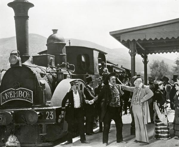 Scena del film "Figaro e la sua gran giornata" - Camerini, Mario, 1931 - Giafranco Giachetti appoggia una mano sulla spalla di un attore non identificato a braccia aperte. Un attore non identificato, a sinistra in abiti da ferroviere, li osserva.