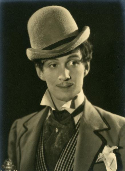 Scena del film "Figaro e la sua gran giornata" - Camerini, Mario, 1931 - Primo piano di Maurizio D'Ancora che, con un cappello a bombetta in testa, rivolge uno sguardo sorridente verso destra.
