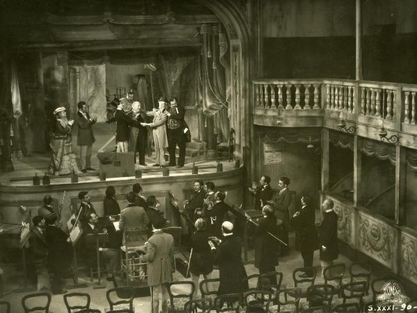 Scena del film "Figaro e la sua gran giornata" - Camerini, Mario, 1931 - Gianfranco Giachetti abbraccia un attore non identificato alla sua sinistra. Attorno, attori non identificati guardano avanti e Gloria Leda e D'Ancora, a sinistra, applaudono.