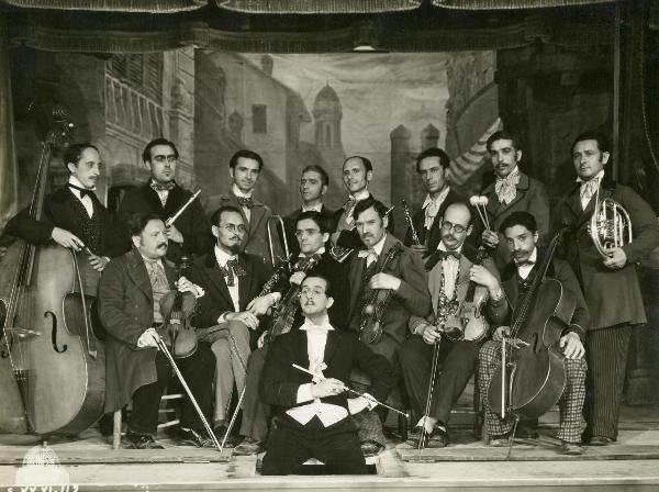 Scena del film "Figaro e la sua gran giornata" - Camerini, Mario, 1931 - Su un palcoscenico, un gruppo di attori non identificati nei panni di un'orchestra.
