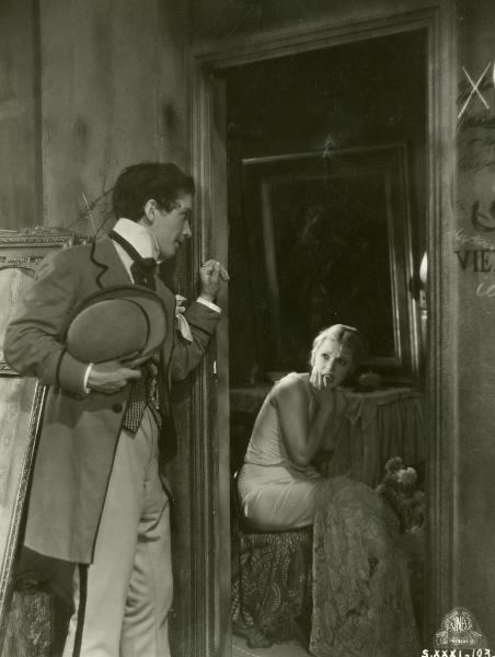 Scena del film "Figaro e la sua gran giornata" - Camerini, Mario, 1931 - Un attore non identificato appoggia la mano sinistra allo stipite di una porta e osserva dentro una stanza in cui è presente un'attrice non identificata che lo guarda.