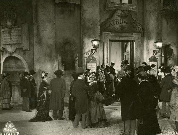 Scena del film "Figaro e la sua gran giornata" - Camerini, Mario, 1931 - Numerosi attrici e attori non identificati, conversano a gruppi in una piazzetta fuori dal Teatro delle Muse.
