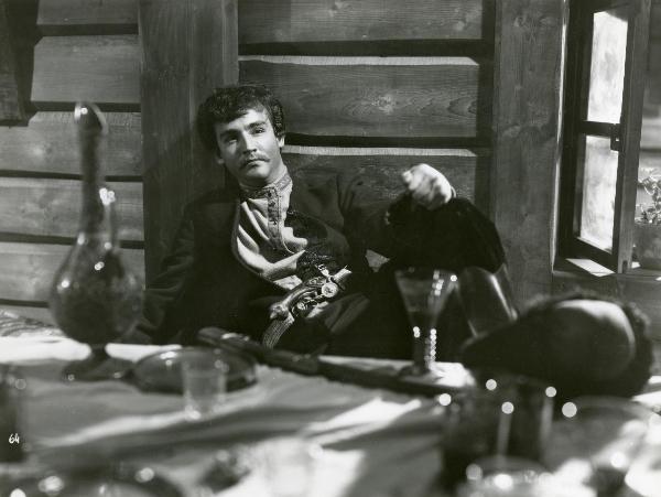 Scena del film "La figlia del capitano" - Camerini, Mario, 1947 - Vittorio Gassman, semidisteso su una branda con una pistola nella cintola, si appoggia il pugno sinistro al ginocchio e rivolge lo sguardo dritto davanti a sé.
