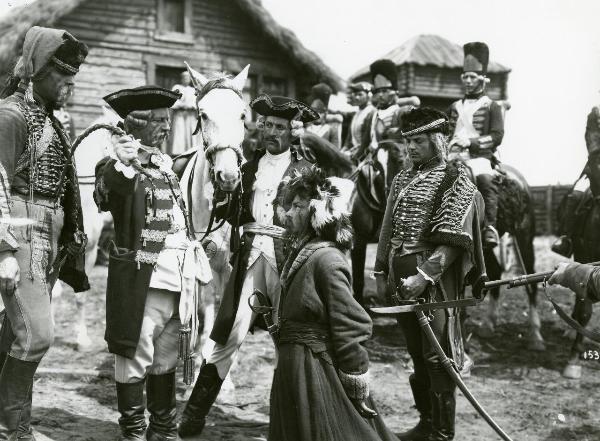 Scena del film "La figlia del capitano" - Camerini, Mario, 1947 - In primo piano, un attore non identificato inginocchiato guarda verso un attore non identificato in piedi che brandisce una cinta intrecciata. Intorno, attori non identificati.