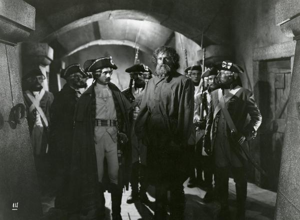 Scena del film "La figlia del capitano" - Camerini, Mario, 1947 - Amedeo Nazzari, al centro, rivolge lo sguardo verso sinistra. Intorno a lui, attori non identificati, in abiti militari, lo guardano.
