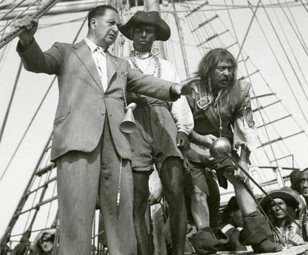 Sul set del film "La figlia del corsaro verde" - Guazzoni, Enrico, 1940 - Camillo Pilotto, a destra con una spada in mano guarda verso destra. Intanto, il regista Guazzoni allunga un braccio in avanti e parla con un attore non identificato al centro.