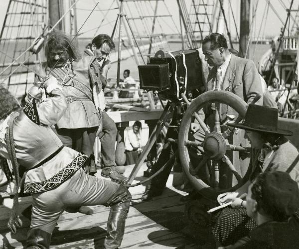 Sul set del film "La figlia del corsaro verde" - Guazzoni, Enrico, 1940 - Mentre Pilotto e un attore non identificato di spalle, a sinistra, simulano un duello con le spade, il regista Enrico Guazzoni e degli operatori non identificati, li osservano.