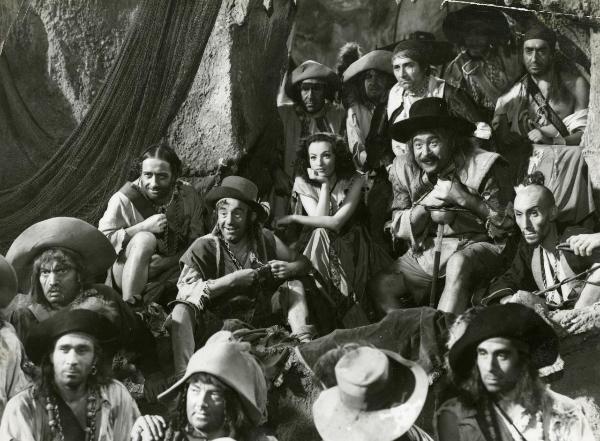 Scena del film "La figlia del corsaro verde" - Guazzoni, Enrico, 1940 - Tra un gruppo di attori non identificati si possono riconoscere: Camillo Pilotto, a sinistra con un cappello a tesa larga, Polidor alla sua sinistra e Doris Duranti, al centro.