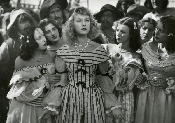 Scena del film "La figlia del corsaro verde" - Guazzoni, Enrico, 1940 - Al centro, Mariella Lotti, a braccia aperte, osserva dritto davanti a sé. Intanto, tre attrici non identificate intorno a lei, insieme a Carmen Navasques, a destra, la osservano.