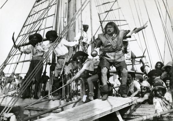 Scena del film "La figlia del corsaro verde" - Guazzoni, Enrico, 1940 - Durante un abbordaggio, molti attori non identificati, in secondo piano in vesti piratesche, si sporgono in avanti. Intanto, al centro, Camillo Pilotto avanza su una passerella.