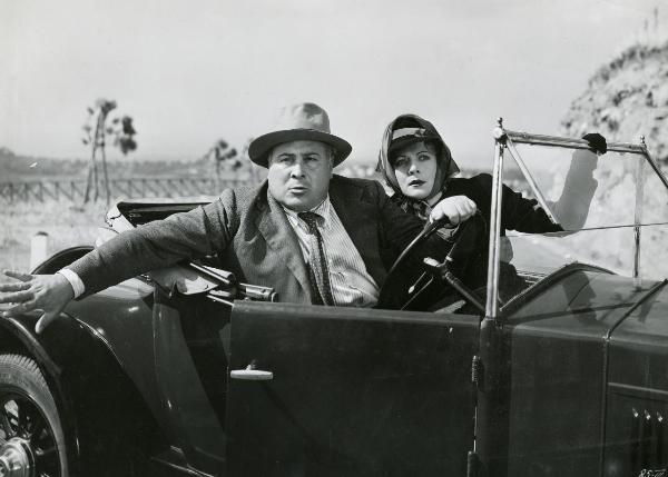 Scena del film "I figli del Marchese Lucera" - Palermi, Amleto, 1938 - In un'autovettura, Camillo Pilotto, alla guida, apre la portiera con una mano e guarda verso l'obbiettivo mentre Gemma Bolognesi rivolge lo sguardo verso destra.
