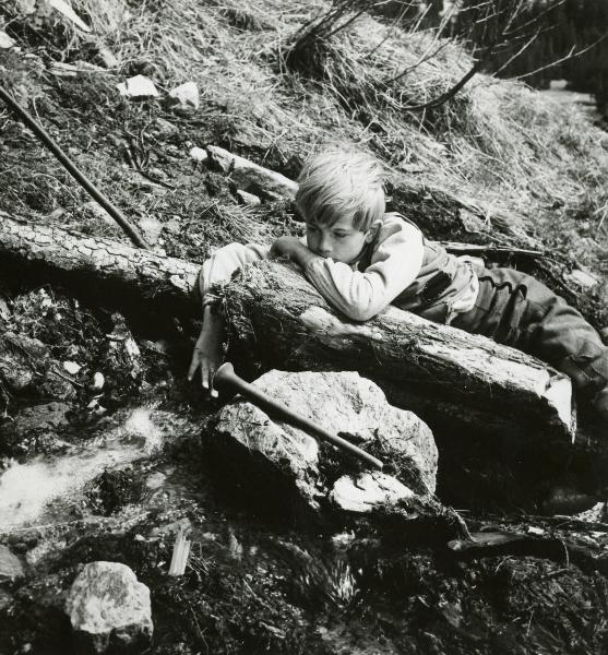 Scena del film "Un flauto in paradiso" - Gamma, Vincenzo, 1958 - Un attore bambino è sdraiato lungo un tronco di un albero vicino a un ruscello.