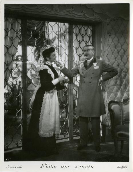 Scena del film "Follie del secolo" - Palermi, Amleto, 1939 - Armando Falconi, in piedi a fianco della finestra, tocca il mento a Clelia Matania in piedi di fianco a lui.

