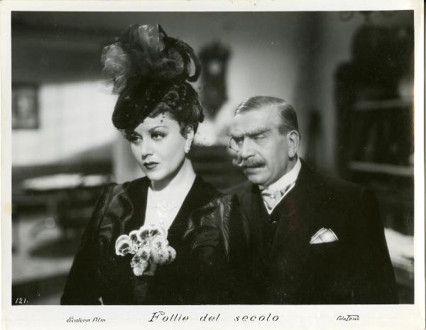 Scena del film "Follie del secolo" - Palermi, Amleto, 1939 - Paola Barbara e Armando Falconi in primo piano, vicini. Lei guarda davanti a sé mentre l'uomo guarda verso di lei con espressione corrucciata.
