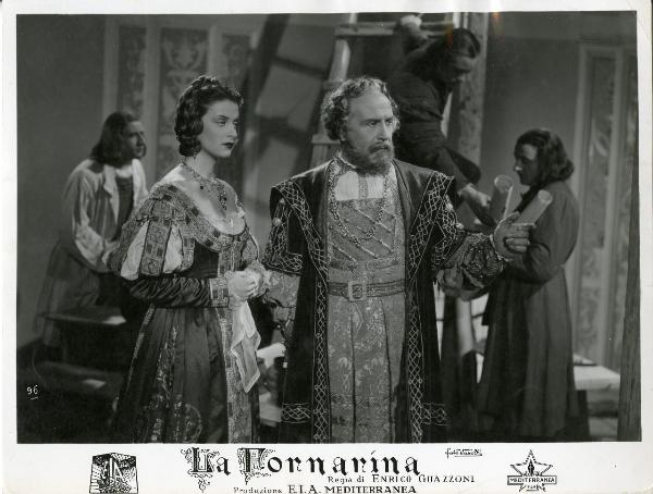 Scena del film "La fornarina" - Guazzoni, Enrico, 1942 - Luigi Pavese guarda a destra e indica con un dito qualcosa che, probabilmente, vede anche Anneliese Uhlig che, con le braccia conserte, osserva.

